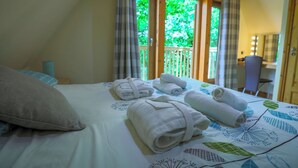 A hotel room with a bed, towels, a window with curtains, and a view of greenery outside. - Lodge 68 - Fern Gully (Newton Abbot)