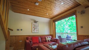 A cozy room with a wooden ceiling, a red leather sofa, and a window with a view of greenery. - Lodge 68 - Fern Gully (Newton Abbot)