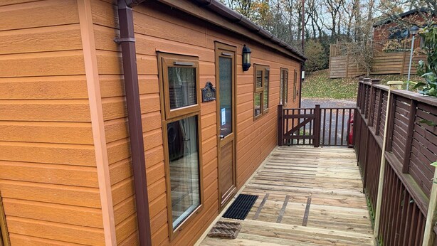 Une cabane en bois dotée d’une terrasse, d’une porte en métal et d’une fenêtre au-dessus de laquelle est accrochée une enseigne.