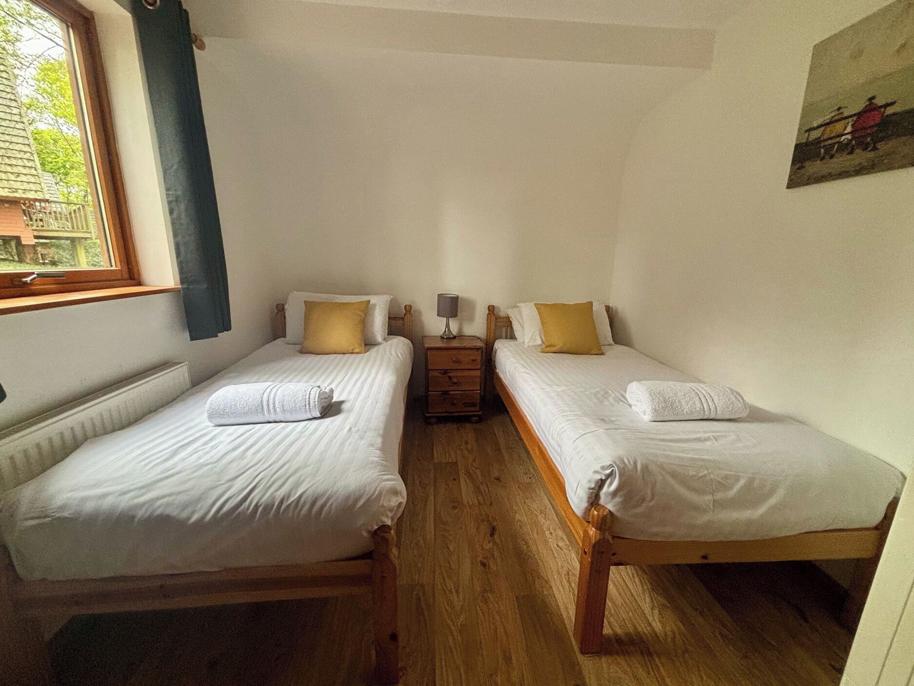 A room with two single beds, a nightstand with a lamp, and a window with curtains.