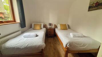 A room with two single beds, a nightstand with a lamp, and a window with curtains.