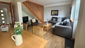 A living room with a wooden staircase, a sofa, a coffee table, and a TV. - Acorn Lodge (Newton Abbot)