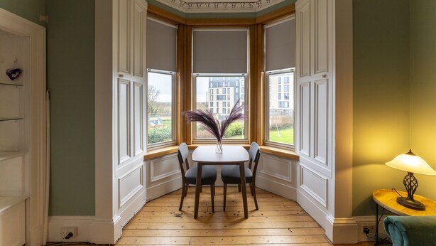 Une pièce d’angle avec une baie vitrée, une table avec des chaises et une lampe.