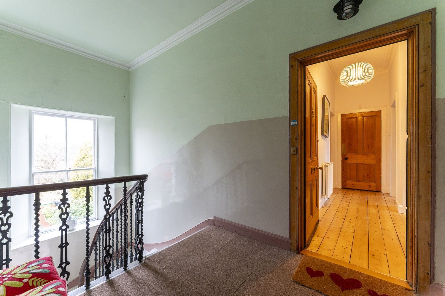 Una escalera con barandilla de madera que conduce a una plataforma, una puerta con marco de madera, y una ventana que da a vistas de follaje.