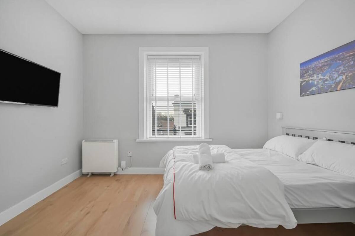 A bedroom with a bed, a radiator, a window with blinds, and a painting on the wall.