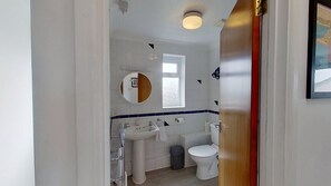 A bathroom with a white sink, a mirror, a toilet, and a window. - F11 Roslyn, Riviere Towans (Hayle)