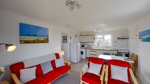 A compact living space with a kitchenette, a dining area with a table and chairs, and a sofa with cushions.