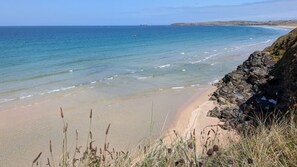 A coastal beach with clear waters, a rocky shoreline, and sparse vegetation. - F11 Roslyn, Riviere Towans (Hayle)