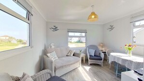 Ein gemütliches Zimmer mit einer Couch, einem Sessel, einem Tisch und einem Fenster mit Blick ins Grüne.