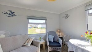 Ein gemütliches Zimmer mit einer Couch, einem Korbstuhl, einem kleinen Tisch und Blick ins Freie.