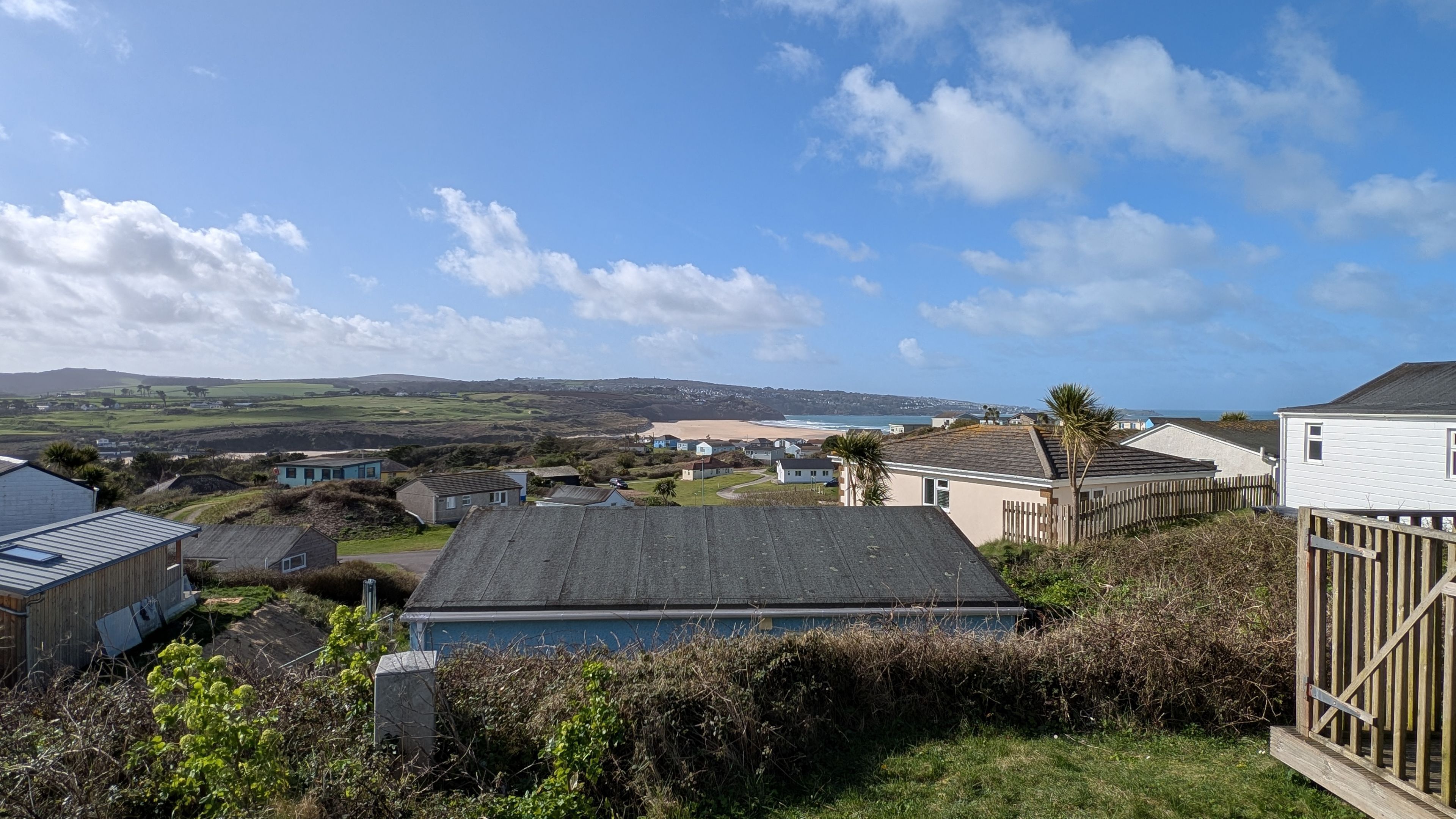 A coastal residential area with houses, a beach, and hills in the background.