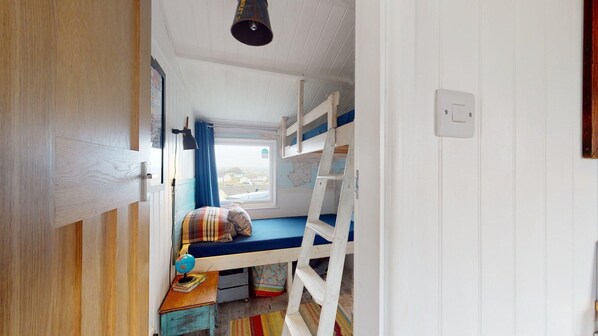 A compact room with bunk beds, a small table with a globe and books, a ladder, and a window with curtains.
