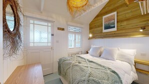 A bedroom with a wooden ceiling, a bed with white bedding, a woven wall hanging, and a window with a view. - F12 West View, Riviere Towans (Hayle)