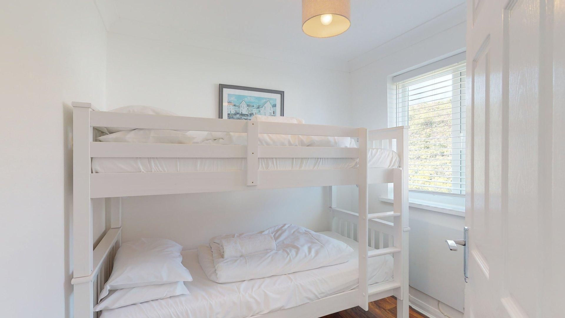 A bunk bed room with a window, a door, and a framed picture on the wall.