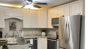 A modern kitchen with white cabinetry, stainless steel appliances, and a dining area with white chairs. - Riverside Retreat at Cades Cove Landing-Unit 250 in Enchanting Townsend, TN (Townsend)