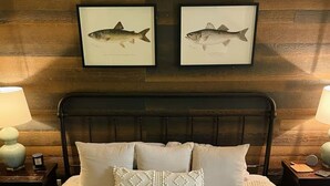 A neatly made bed with a textured white duvet, flanked by two bedside tables with lamps, and framed fish illustrations on the wall above. - Riverside Retreat at Cades Cove Landing-Unit 250 in Enchanting Townsend, TN (Townsend)