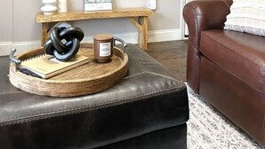 A living room with a mounted flat-screen TV, a wooden side table with decorative items, a brown leather couch, and a patterned rug. - Riverside Retreat at Cades Cove Landing-Unit 250 in Enchanting Townsend, TN (Townsend)