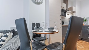 A modern kitchen with a dining area, featuring a round table with chairs, a clock, and a plant. - Modern Leeds city centre 2BR Apt - sleep 8 (leeds)