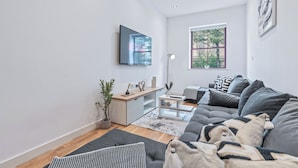 A modern living room with a grey sofa, a flat-screen TV mounted on the wall, a small coffee table, and a potted plant. - Modern Leeds city centre 2BR Apt - sleep 8 (leeds)