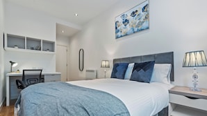 A bedroom with a large bed, a desk, and a chair. There is a painting on the wall and a lamp on the nightstand. - Modern Leeds city centre 2BR Apt - sleep 8 (leeds)