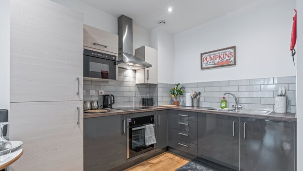 A modern kitchen with grey cabinets, stainless steel appliances, and a wooden floor. - Modern Leeds city centre 2BR Apt - sleep 8 (leeds)