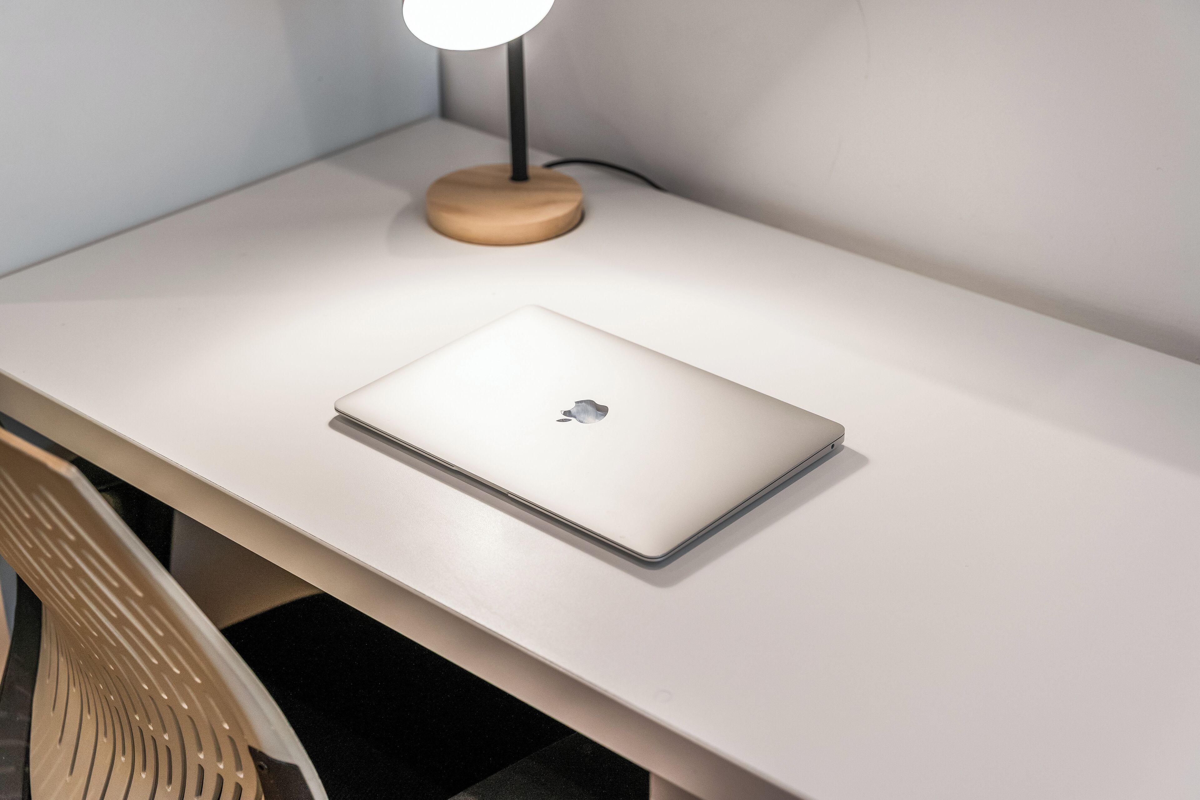 Um laptop sobre uma mesa branca com uma luminária de madeira.