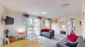 A cozy living room with a sofa, a dining table, and a TV mounted on the wall. - 58 Trevithick Court, Tolroy Manor (Hayle)