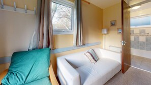 A room with a bed, a sofa, a window with curtains, a lamp, and a view of the outside.