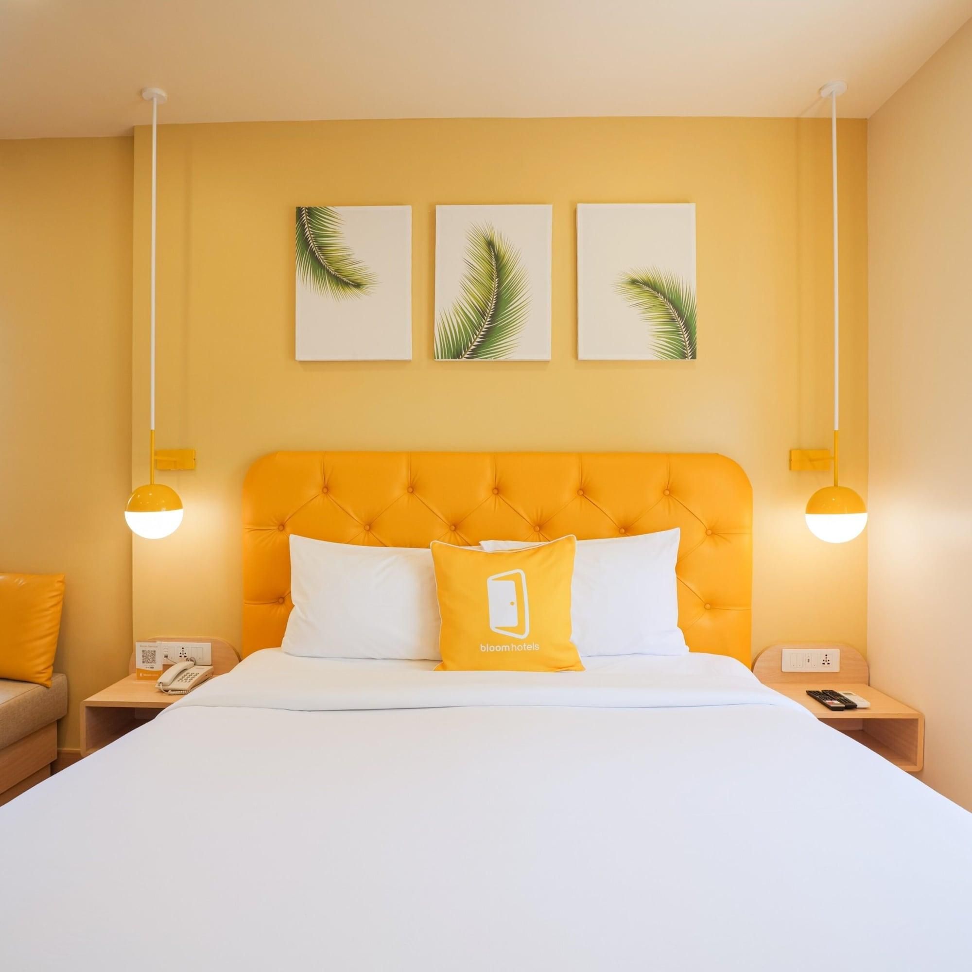 A hotel room with a tufted orange headboard, white bedding, and three palm leaf wall art pieces.