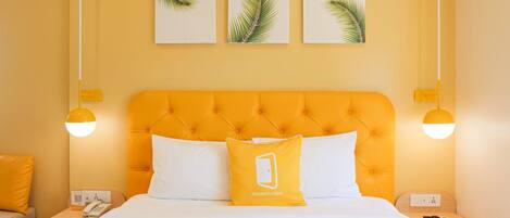 A hotel room with a tufted orange headboard, white bedding, and three palm leaf wall art pieces.