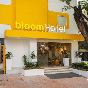 A hotel entrance with a yellow facade, a glass door, and potted plants.