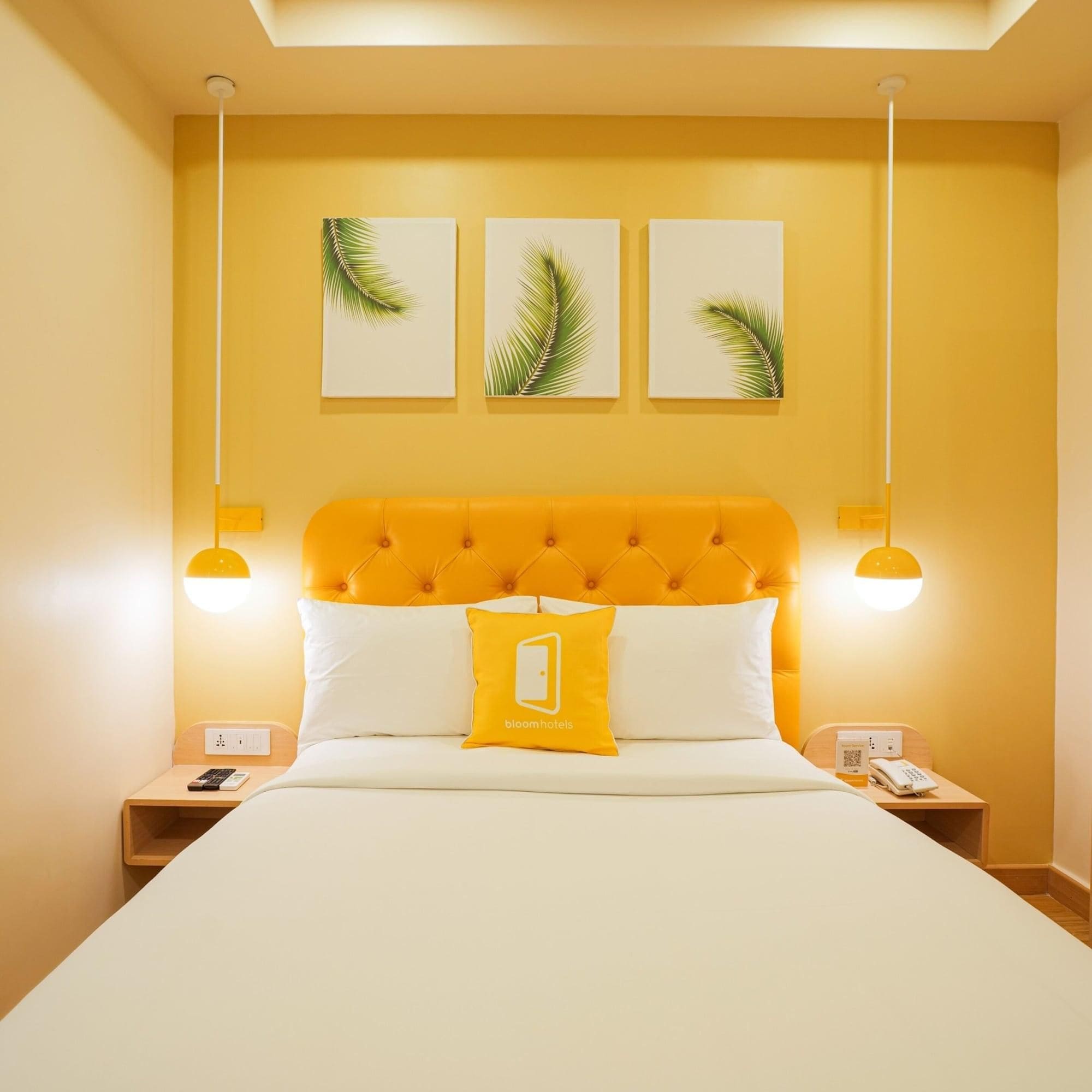 A hotel room with a yellow headboard, white bedding, and three palm leaf wall art pieces.