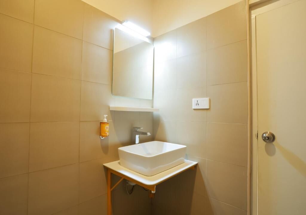 A bathroom with a white sink, a mirror, and a soap dispenser.