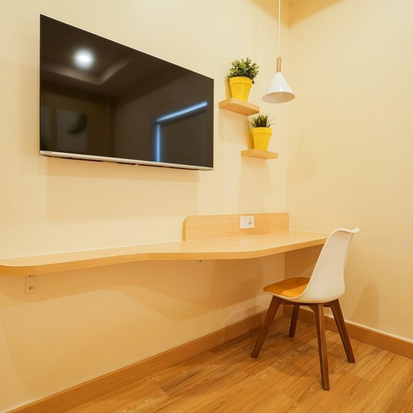 A modern room with a flat-screen TV mounted on the wall, a wooden desk with a chair, and two potted plants on floating shelves. - Bloom Hotel - Koramangala (Bengaluru)