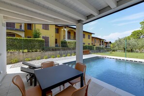 A covered outdoor area with a pool, a table, and chairs.