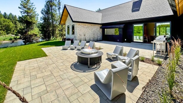 A modern outdoor patio with a fire pit, lounge chairs, and a stone building in the background.