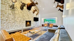 A modern living room with a stone wall, a fireplace, leather sofas, and mounted animal heads.