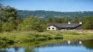 A house by a lake with a forested hill in the background.