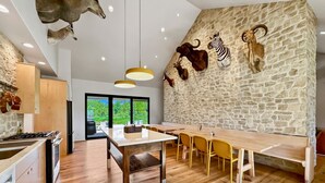 A modern kitchen with a stone wall, wooden flooring, and a dining area with yellow chairs.