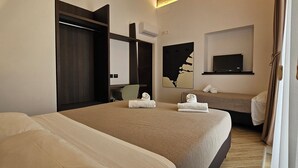 Habitación de hotel con una cama grande, una cama más pequeña, un escritorio, una silla, un televisor y un cuadro en la pared.