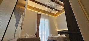 Habitación de hotel con dos camas, una pared de acento de piedra, ventilador de techo y un gran ventanal con cortinas.