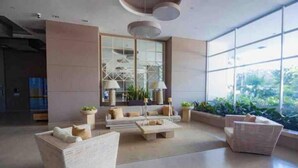 A spacious lobby with a modern sofa set, a coffee table, and a wicker chair. There are potted plants and a large window providing a view of greenery outside. - Reserva del Mar: Condominium with Ocean View (Santa Marta, Gaira)