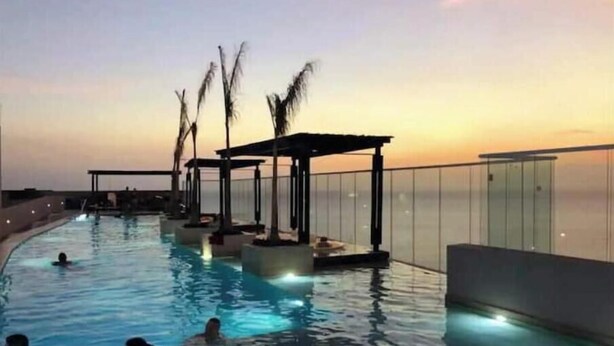 An infinity pool with a sunset view, palm trees, and a covered seating area. - Reserva del Mar: Condominium with Ocean View (Santa Marta, Gaira)