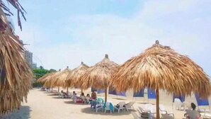 A beach with thatched umbrellas and white lounge chairs. - Reserva del Mar: Condominium with Ocean View (Santa Marta, Gaira)
