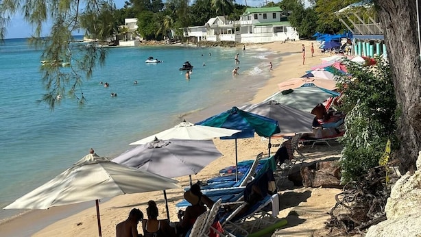 A beach with clear blue water, lounge chairs, umbrellas, and a few people.