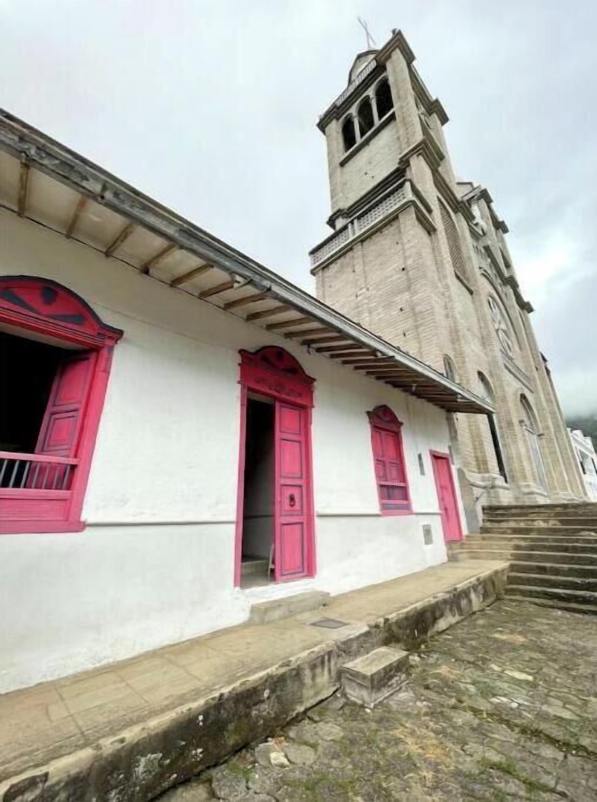 A building with a white facade and red window shutters, a stone staircase, and a tall tower with arched windows.