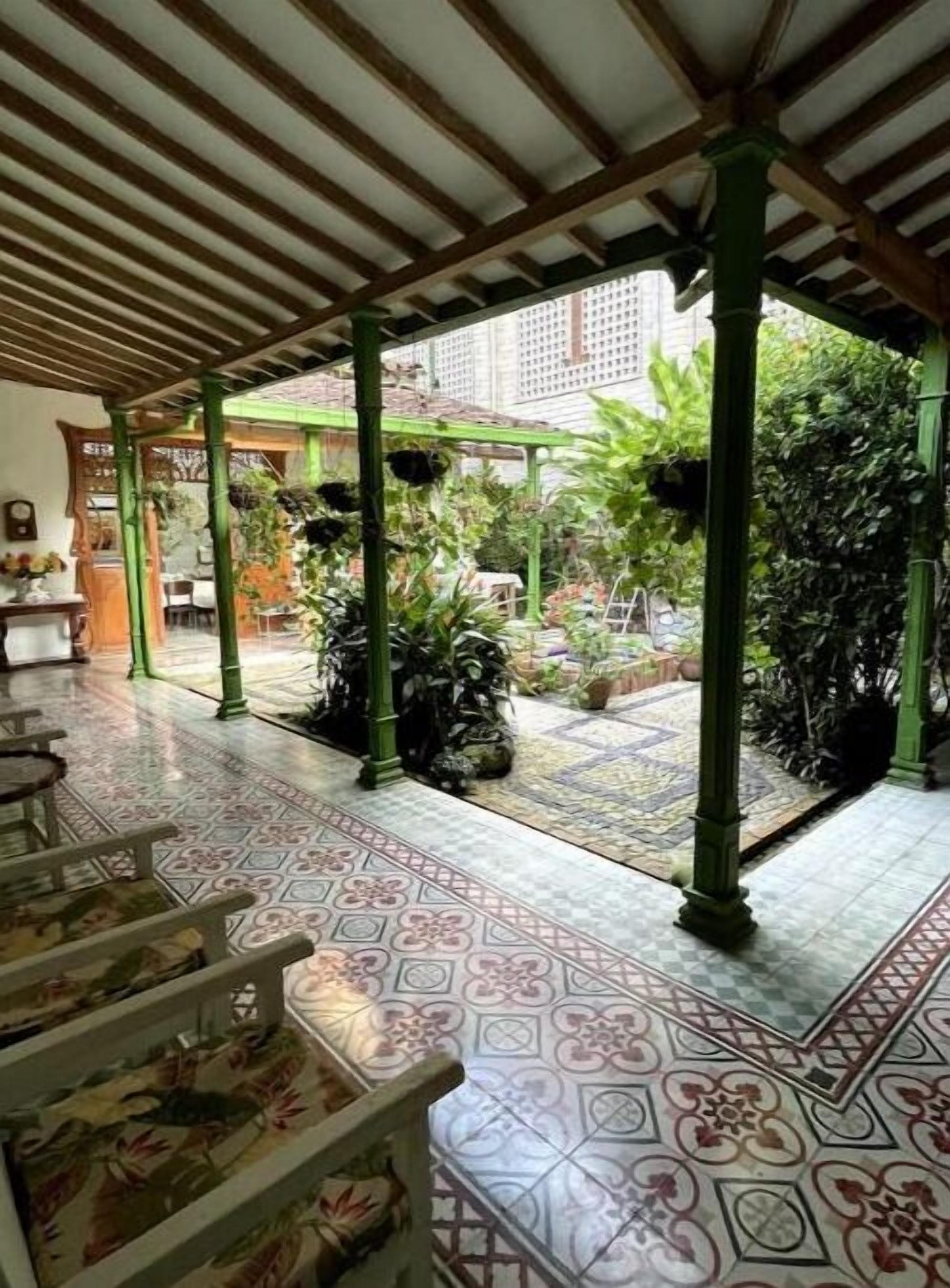 A covered outdoor area with tiled flooring, green pillars, and potted plants.