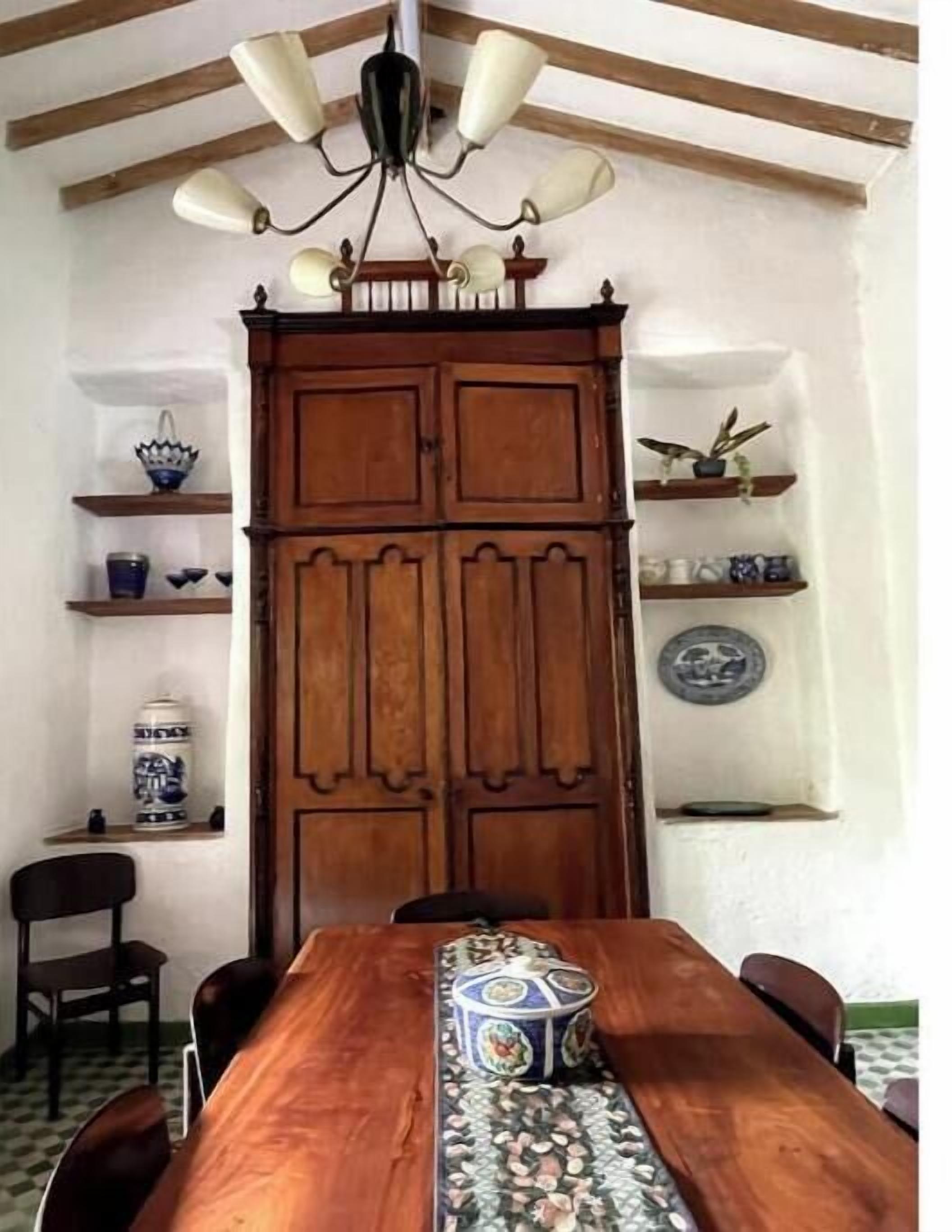 A dining area with a wooden table, chairs, a chandelier, and shelves with decorative items.
