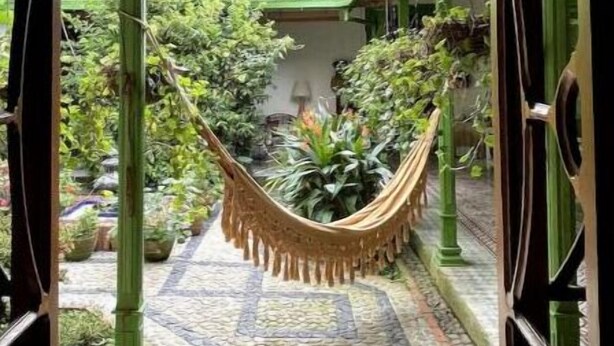 An entrance with a wrought iron gate, a hammock, and a tiled pathway leading to a building with a tiled roof.