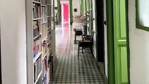 A narrow hallway with a checkered floor, green doors, and a bookshelf on one side.